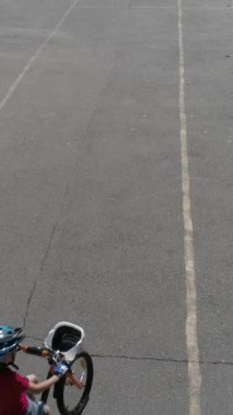 Şehir parkında bisikletle gezen aktif bir çocuğun havadan görünüşü. Çocukluk eğlence aktivitesi ve spor. Dikey video.