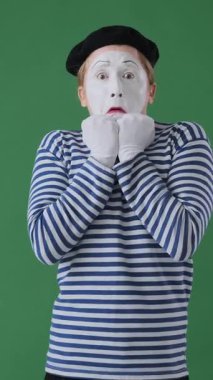 Yeşil arka planda korkmuş pandomimci bir adamın portresi. Gergin ve etkileyici bir tavırla şoka giriyor ve başarısız oluyor. Dikey video.