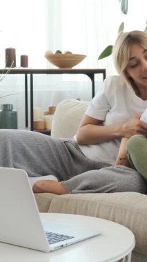 Mutlu anne ve okul çocuğu evde birlikte online bir program izlemek için dizüstü bilgisayar kullanıyor, neşeli bir evde paylaşılan dijital eğlenceye katılıyorlar. Dikey video.