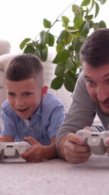 Mutlu oğul ve baba evdeki gamepad 'leri kullanarak oyun oynuyorlar, canlı bir atmosferde boş zamanlarında rekabete giriyorlar ve bağ kuruyorlar. Dikey video.