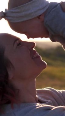 Anne gün batımında kızıyla dışarıda oynuyor, doğal bir manzarayla çevrili, huzurlu ve neşeli bir ortamda yürüyüş yapıyor ve kaynaşıyor. Dikey video.