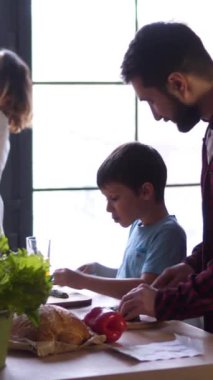 Geniş aile evde mutfakta birlikte taze bir yemek hazırlıyor, sıcak ve işbirliğiyle hafta sonu yemeklerinin tadını çıkarıyor. Dikey video.