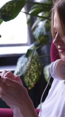 Online eğlence için telefon kullanan, boş zamanlarında evde dinlenen, rahat ve neşeli dijital anın tadını çıkaran tatmin olmuş bir kadın. Dikey video.