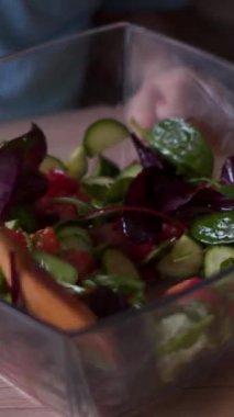 Evdeki mutfaktaki kasede sebze salatasını karıştıran bir çocuğun yemek hazırlığını dikkatle ve dikkatle yaptığı yakın çekim. Dikey video.