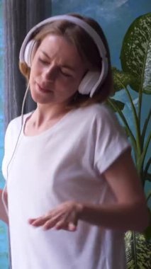 Hafta sonu evde dans eden neşeli ve arkadaş canlısı bir kadın neşeli hareketlerle dolu bir parti atmosferinden zevk alıyor. Dikey video.