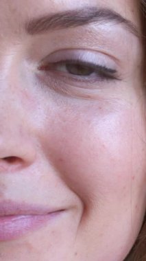 Beyaz bir arka planda bir kadının yüz ve göz portresi, doğal güzelliği ve zarafeti sakin ve büyüleyici bir ifadeyle sergiliyor. Dikey video.