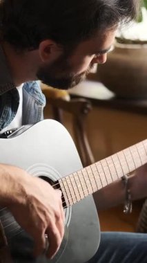 Evde gitar çalan, boş zamanlarında dinlenen, müziğin keyfini çıkaran ve rahat ve huzurlu bir ortamda rahatlık ve keyif bulan bir adam. Dikey video.