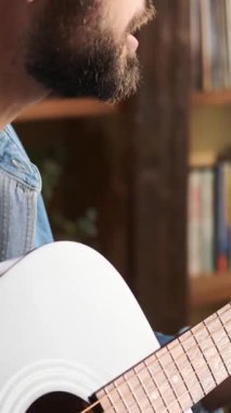 Evde gitar çalan, müzikten zevk alan, rahat ve evcimen bir ortamda beceri ve tutku sergileyen pozitif bir adamın yakın çekimi. Dikey video.
