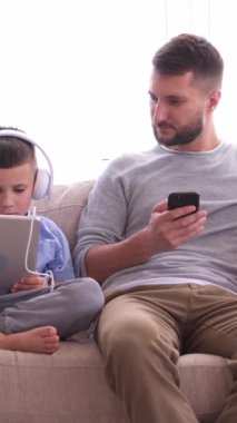 Çocuklu bir aile evde internet eğlencesi ve internet eğlencesi için cihazlar kullanıyor, canlı ve bağlantılı bir dijital deneyime giriyorlar. Dikey video.