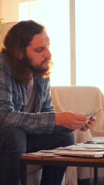 Mutlu adam evde nakit para sayıyor, bütçeyi, maaşı ve geliri düzenliyor, rahat bir ortamda finans yönetirken memnuniyeti yayıyor. Dikey video.