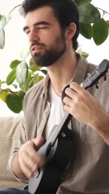 Evde boş zamanlarında gitar çalan ve şarkı söyleyen iyimser bir adam, öğreniyor ve zevk alıyor, tanıdık bir mekanda neşeli bir müzik anı yaratıyor. Dikey video.