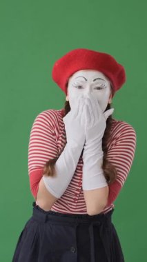 Yeşil arka planda korkmuş bir pandomimci kadın portresi, korku ve dehşete kapılmış duygular sergiliyor, yoğun ve korkmuş bir ifade sergiliyor. Dikey video.