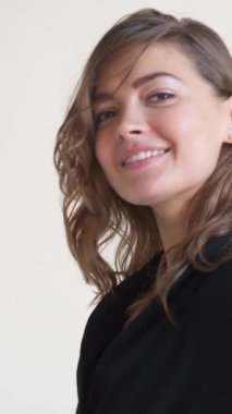 Beyaz arka planda bir portrede şehvetli ve pozitif bir kadın büyüleyici ve canlı bir ifadeyle kadınsı bir zevk ve benzersizlik sergiliyor. Dikey video.