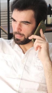 Evdeki bir telefon görüşmesi sırasında sohbet eden, iletişim ve diyalogla vakit geçiren, rahat bir ortama bağlanan tatmin olmuş bir adam. Dikey video.