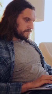 Yoğunlaşmış bir adam evde e-öğrenim ya da sohbet için dizüstü bilgisayar kullanıyor, eğitici iletişim ve odaklanmış bir zihniyetle meşgul oluyor. Dikey video.