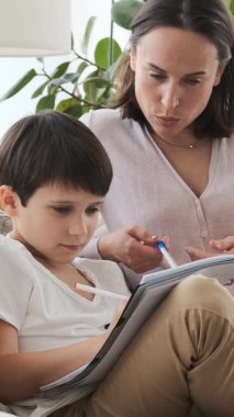 Okul çocuğuyla birlikte olumlu ve ilgili bir anne evde ödev yapıyor, eğitim ve anneliği destekleyici bir ortamda destekliyor. Dikey video.