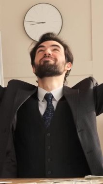 Başarıyı kutlayan adam ofise nakit para saçarak, lüks ve refahı kucaklayarak, profesyonel bir çalışma alanında muzaffer bir finansal anı işaret ederek kutluyor. Dikey video.