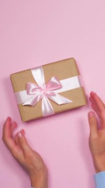 Hediye kutusu ve pembe arka planda kurdelesi olan bir kadının üst görüntüsü. Özel bir durum için sürpriz bir paket sunuyor. Dikey video.