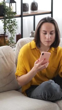 Mutlu bir kadın evdeki video görüşmesi ve sohbeti için telefonunu kullanıyor. Bağlantı kuruyor ve samimiyet ve coşkuyla tartışıyor. Dikey video.