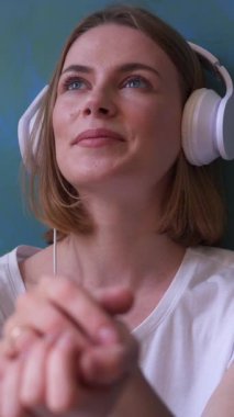 Heyecanlı bir kadın eğlence sırasında dinleniyor, kulaklıkla müzik dinliyor, neşeli ve ferahlatıcı bir aktiviteye girişiyor. Dikey video.