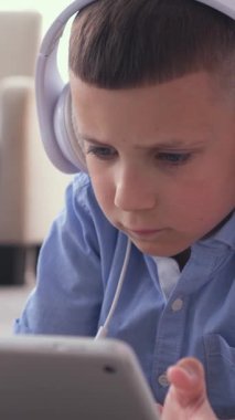 Evde boş zamanlarında bir tablet bilgisayar kullanarak çevrimiçi video oyunu oynayan, kendini sıcak bir ortama adamış bir çocuk. Dikey video.