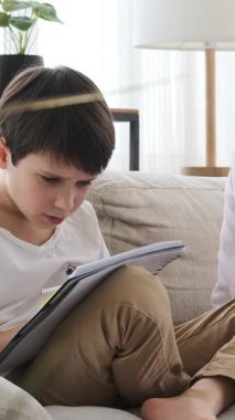 Ciddi bir anne internette çalışırken oğlu evde ödev yapıyor, disiplinli bir ortamda eğitim ve öğrenimi dengeliyor. Dikey video.