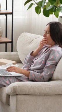 Evde dizüstü bilgisayar kullanırken öksüren ve hapşıran hasta bir kadın, dikey bir çerçevede grip ve virüs semptomlarıyla baş etmek, hastalık sorunlarını yansıtıyor. Dikey video.