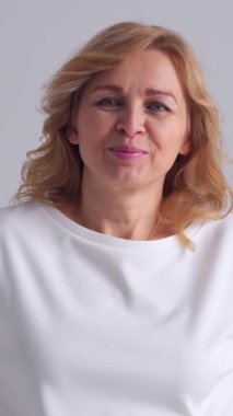 Beyaz bir arka planda rahat ve cana yakın bir kadın, sıcak ve cana yakın bir ifadeyle şık bir kişilik ve kadınlık sergiliyor. Dikey video.