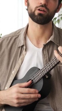 Dost canlısı bir adam evde boş zamanlarında gitar çalıp şarkı söylüyor, müzik ve zevkin tadını çıkarıyor, tanıdık bir ortamda sıcak ve yaratıcı bir meşgale ile meşgul oluyor. Dikey video.