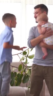 Evde boş zamanlarında müzik eşliğinde dans eden iki çocuklu baba neşeli ve neşeli bir aile ortamında birlikte eğleniyor. Dikey video.