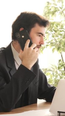 Ofisteki bir tüketiciyle telefonda iş görüşmesi yapan profesyonel bir çalışan, yapılandırılmış bir ortamda işle ilgili tartışmaları uzmanlıkla yürütüyor. Dikey video.