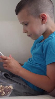 İnternette gezinen mutlu bir çocuk ya da evinde bir tabletle online eğlencenin tadını çıkaran, canlı ve büyüleyici bir dijital zevke dalmış bir çocuk. Dikey video.