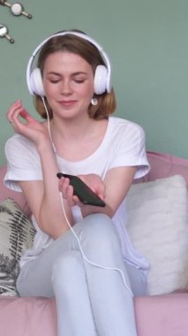 Neşeli ve mutlu bir kadın evde müzik dinleyerek eğleniyor, rahat bir ortamda keyifli bir eğlenceyi kucaklıyor. Dikey video.