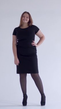 Beyaz bir arkaplanda portrede zarif ve memnun bir kadın. Kişilik, bireysellik ve hazzı dengeli ve tatmin edici bir tavırla sergiliyor. Dikey video.