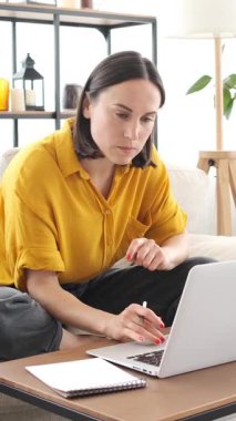 Yoğunlaşmış bir kadın evde çalışmak ya da e-öğrenim için dizüstü bilgisayar kullanıyor, odaklanmış bir strateji geliştiriyor. Dikey video.