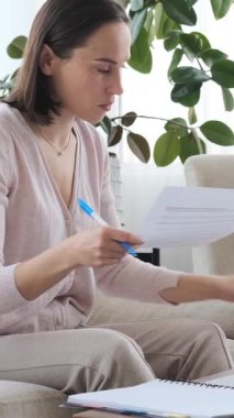 Evde mali belgelerle uğraşan bir kadın, yakınlardaki bir telefonla meşgul olurken, işine odaklanmış bir çevrede çalışan bir çocuk. Dikey video.