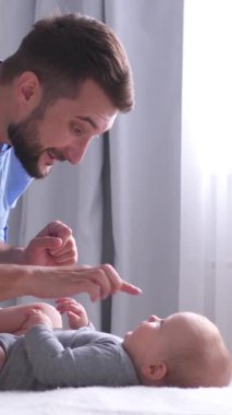 Dost canlısı bir baba rahat aktivitelerden ve küçük bebekle rahat bir yatak odasında oyun oynamaktan hoşlanır. Mutluluk ve refah kavramı. Dikey video.