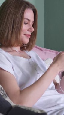 Dijital bir eğlenceye katılan, evde müzik dinleyen, sakin bir ortamda huzurlu ve neşeli bir deneyimi kucaklayan pozitif bir kadın. Dikey video.