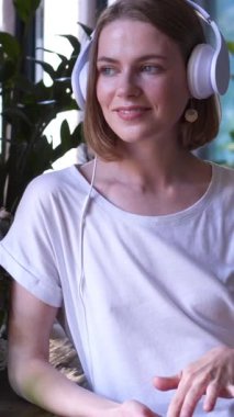 Neşeli bir kadın evde müzik dinliyor ve dinleniyor. Huzurlu bir ortamda tatmin ve eğlence arıyor. Dikey video.