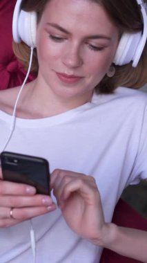 Memnuniyet verici bir kadın cep telefonunu evdeki internet eğlencesi için kullanıyor, neşeli ve ilgi çekici bir dijital ortamda iletişimle rahatlıyor. Dikey video.