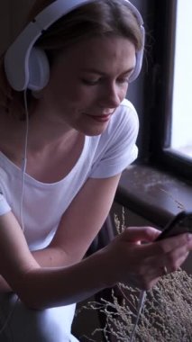 İnternet ve online eğlence için akıllı telefon kullanan, evde boş zamanlarında müzik dinleyen, canlı bir dijital deneyimin tadını çıkaran göz alıcı bir kadın. Dikey video.
