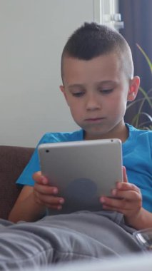 Neşeli çocuk evde internet keyfi ve online eğlence için tablet bilgisayar kullanıyor, canlı ve neşeli bir dijital siber ortama bağlanıyor. Dikey video.