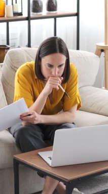 İnternette çalışan konsantre bir kadın ve evde bir müşteriyle telefon görüşmesi yapıyor. Profesyonel odaklı konuşmaları yönetiyor. Dikey video.