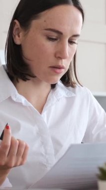 Ofisteki kadın ofis çalışanı bir dizüstü bilgisayar ve evrak işleriyle bir ofiste muhasebe yapıyor. İfadeleri dikkatle ve titizlikle inceliyor. Dikey video.