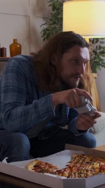 Video oyunu oynayan odaklanmış bir adam, evde eğlenirken kazandığı zaferi kutlayan, dijital eğlenceye heyecan ve memnuniyet katan. Dikey video.