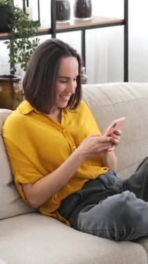 Dost canlısı bir kadın evdeki sosyal medyada mesajlaşmak için telefon kullanıyor, dijital iletişimi devreye sokarak iletişimi teşvik ediyor. Dikey video.