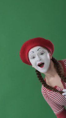 Neşeli bir kadın yeşil arka planda selamlaşma pandomimcisi sallıyor, sıcaklığı ve nişanı ifade etmek için davetkar jestler yapıyor. Dikey video.