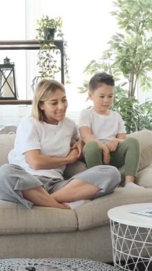 Okul çocuğu ve annesi birlikte çizgi film seyrediyor, evde online eğlenceye dalmış, rahat bir ortamda eğlenceli ve çekici anları paylaşıyorlar. Dikey video.