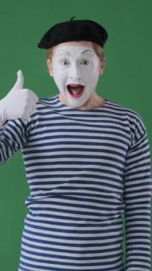 Tatmin olmuş pandomimci adam yeşil arka planda bir işaret gibi kendinden emin bir hareketle memnuniyetini ifade ediyor. Dikey video.