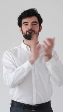 Mutlu bir adam beyaz bir arkaplanı alkışlıyor. Basit bir ortamda saygı, tebrik ve takdir gösteriyor. Dikey video.